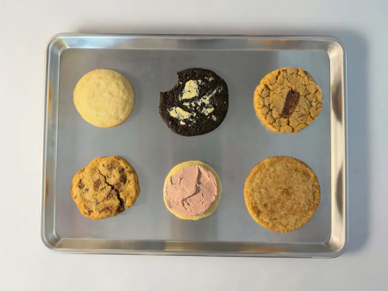 Six different Misfit cookies arranged on a baking tray against a white background.