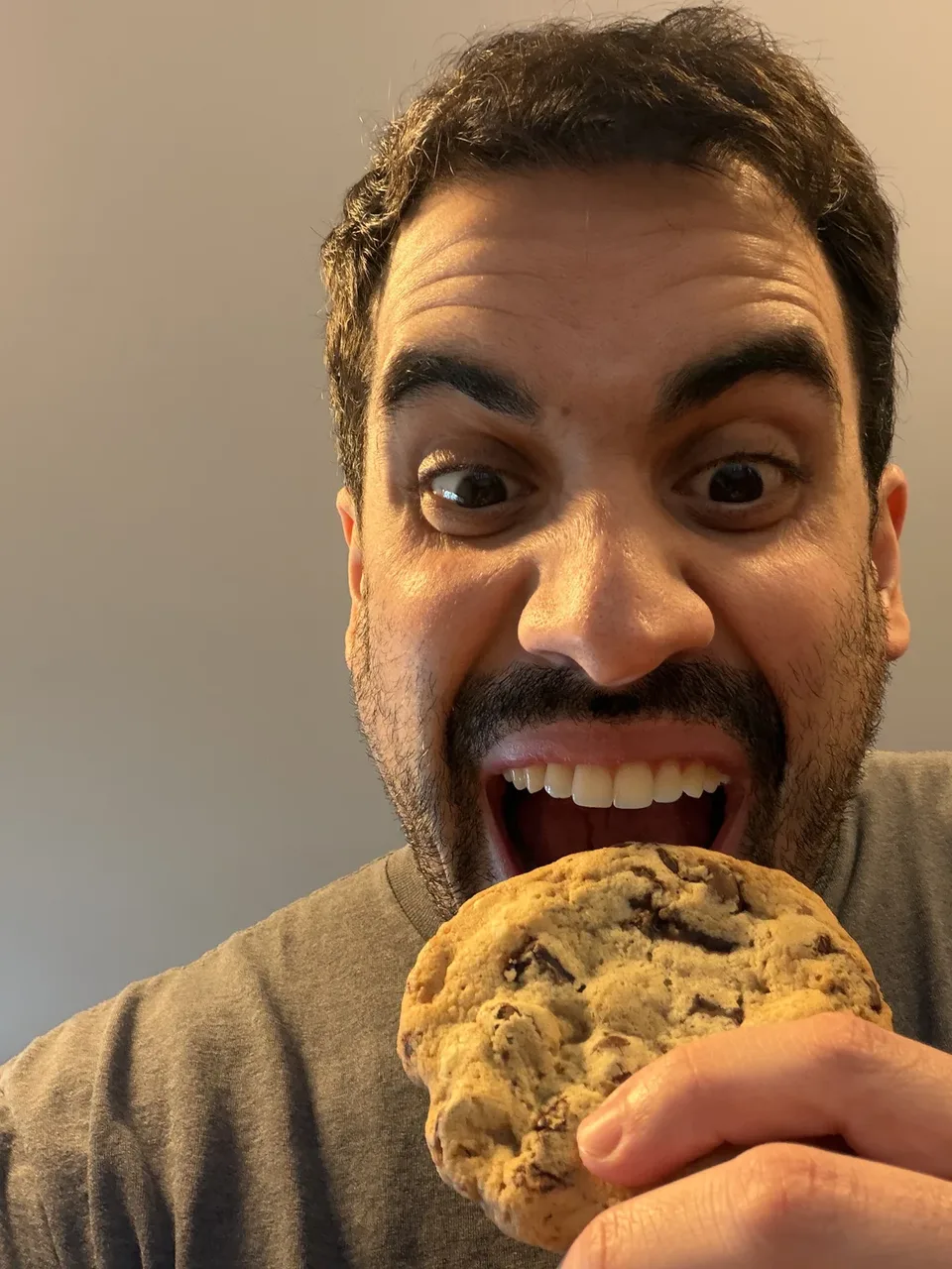A person about to take a bite of a chocolate chunk cookie.